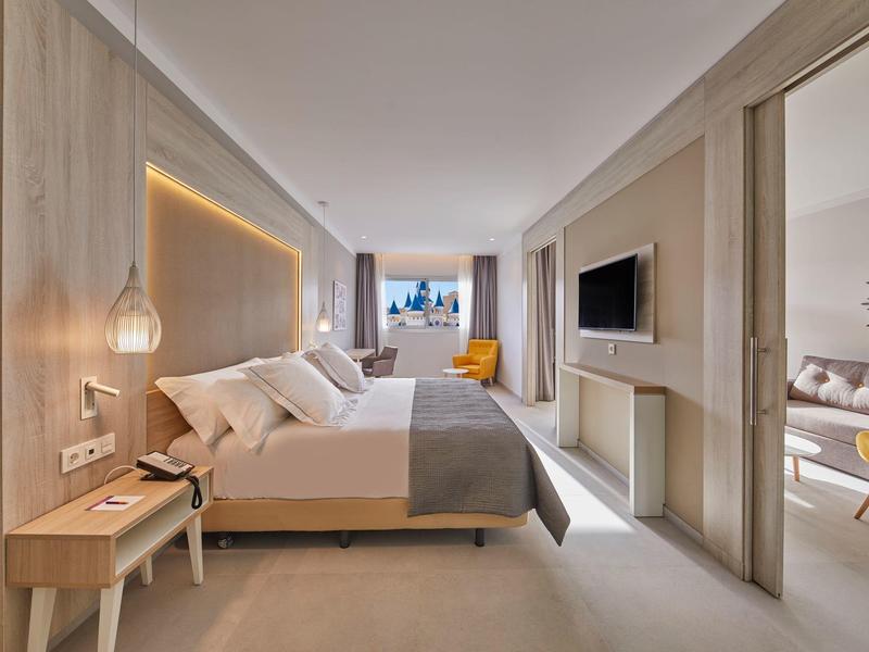 Moderní hotelový pokoj s velkou postelí, pracovním stolem, televizí a výhledem z okna.