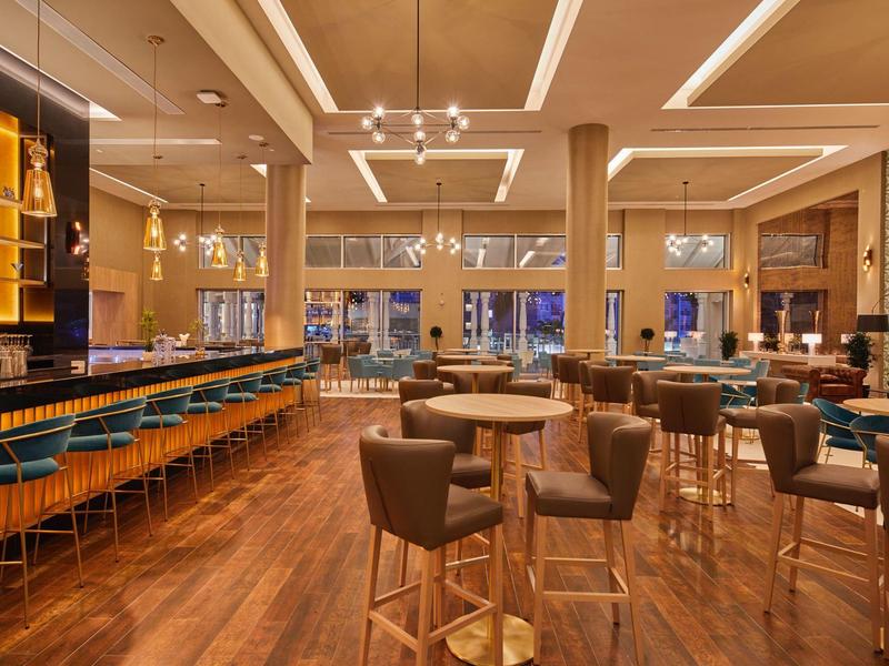 Elegantní hotelový bar s vysokými židlemi, dřevěnou podlahou a moderním osvětlením.