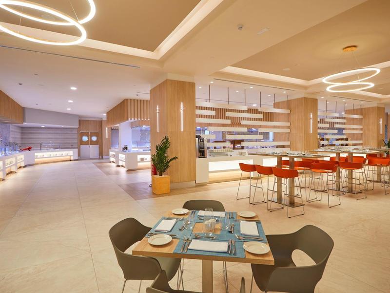 Moderní hotelová restaurace se stylovým osvětlením a stoly s modrými prostíráními.