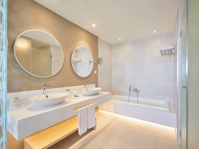 Světelná koupelna se dvěma umyvadly, kulatými zrcadly a vanou.