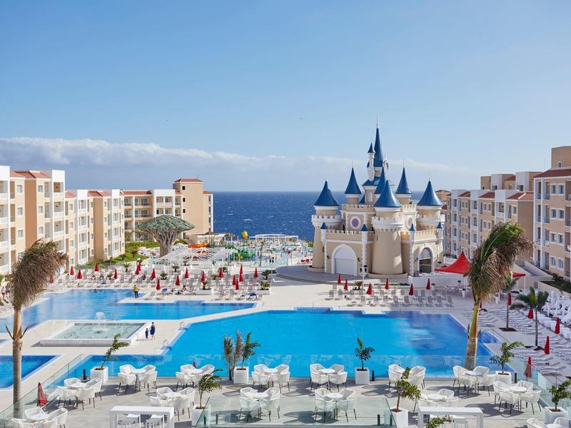 Velké hotelové středisko s bazény, atrakcí zámku a výhledem na moře pod jasnou oblohou.