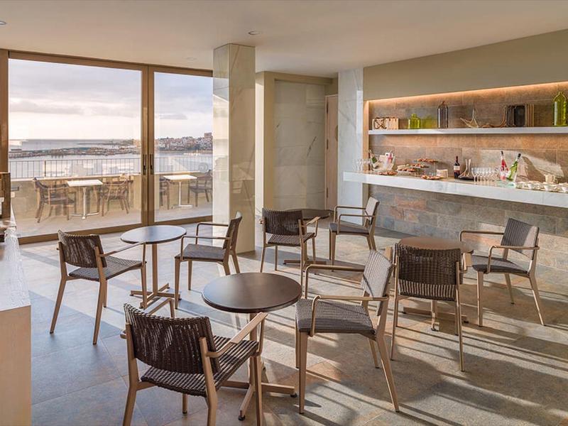 Helles Café mit Holzstühlen, Tischen und großem Panoramafenster mit Meerblick.