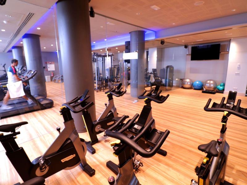 Moderne Fitnessstudio mit Spinningrädern, Laufband, Holzfußboden und großen Fenstern.