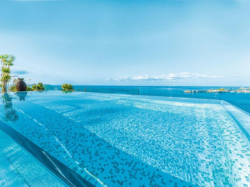 Ein großer, blauer Infinity-Pool mit Blick auf das Meer und den klaren Himmel.