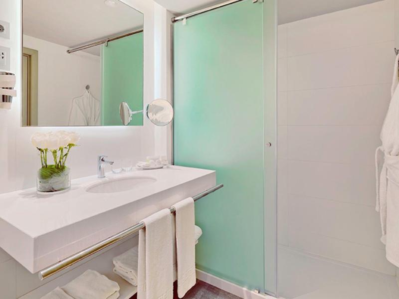 Helles Badezimmer mit weißem Waschbecken, grün getönter Duschkabine und Handtüchern.