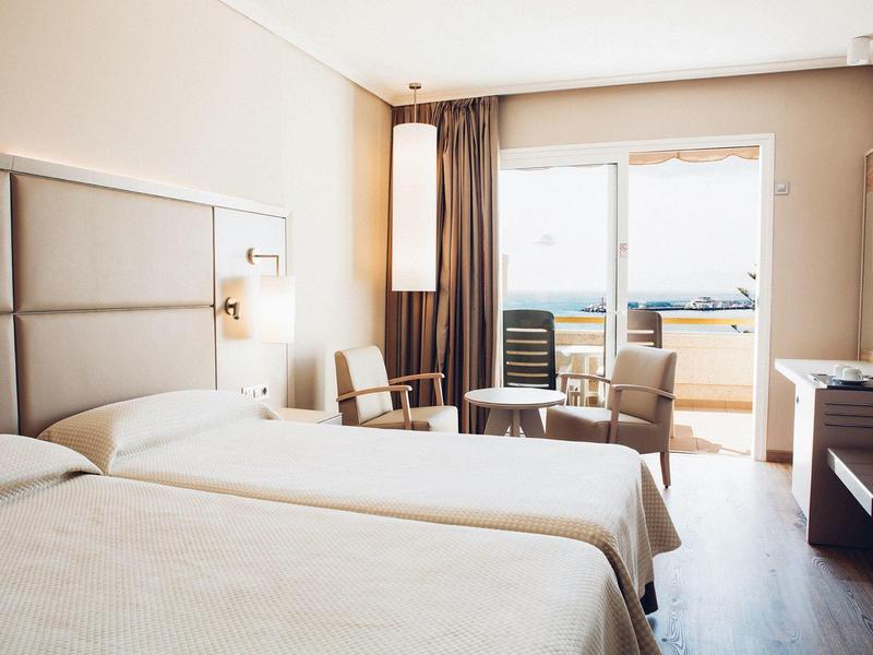 Hotelzimmer mit zwei Einzelbetten, Stühlen, Tisch, Balkon und Fenster mit Tageslicht.