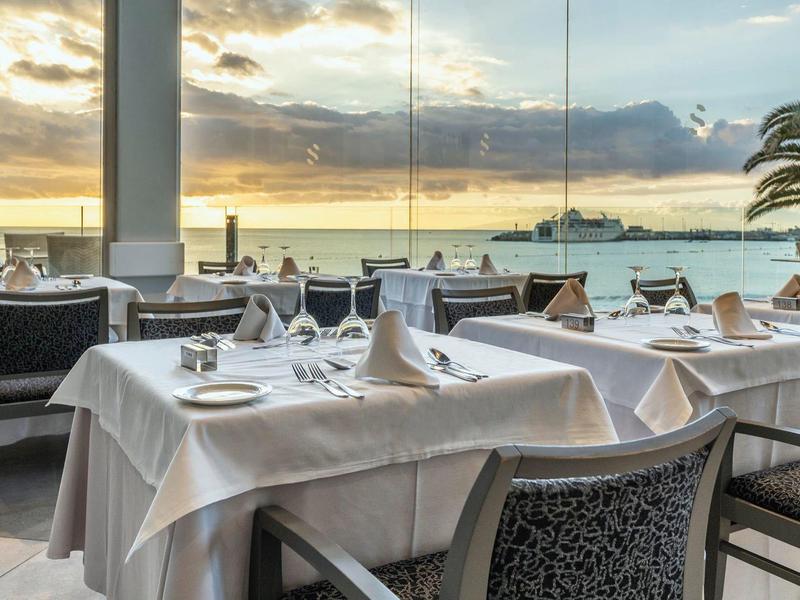 Tisch mit weißer Tischdecke und gedecktem Besteck im Restaurant mit Meerblick und Sonnenuntergang.