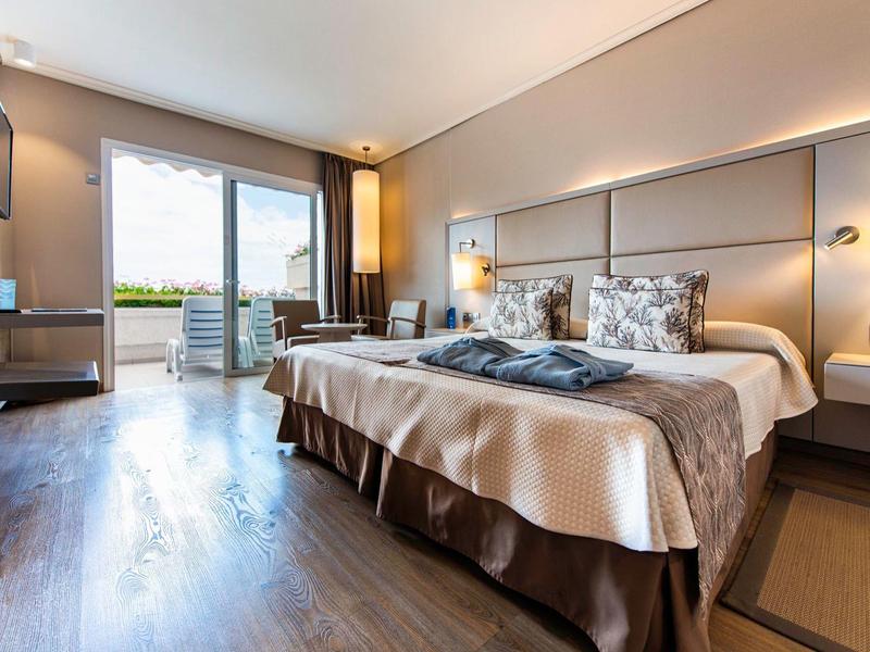 Modernes Hotelzimmer mit Doppelbett, Holzboden, Balkon und gemütlicher Beleuchtung.