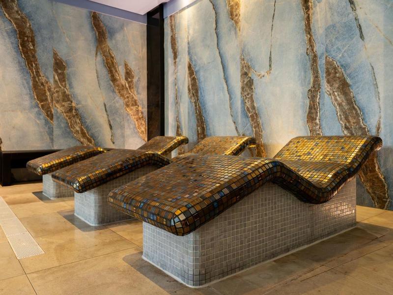 Moderne Ruhezone mit braunen Mosaikliegen vor Wand mit blau-goldenem Muster in hellem Raum.