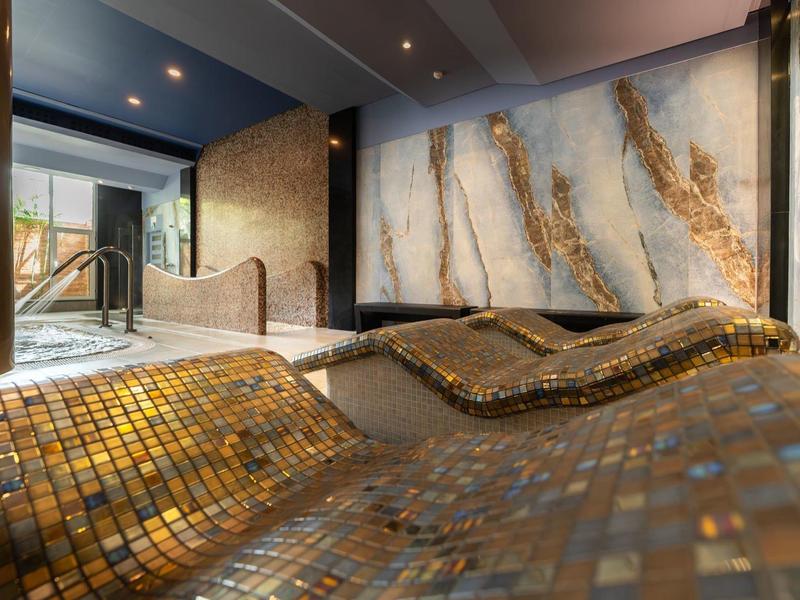 Innenraum mit geschwungenen Mosaikfliesenbänken und heller Wandgestaltung mit goldenen Akzenten.