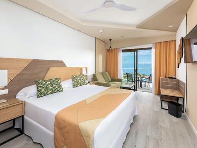 Moderne hotelkamer met groot bed, zithoek en balkon met uitzicht op de oceaan.