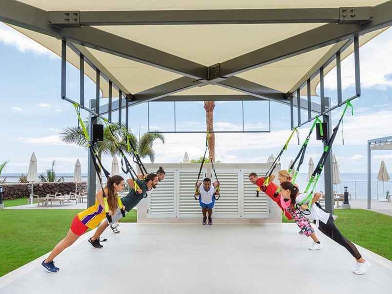 Mensen die trainen met TRX-riemen in een overdekte buitenruimte bij een strandresort.