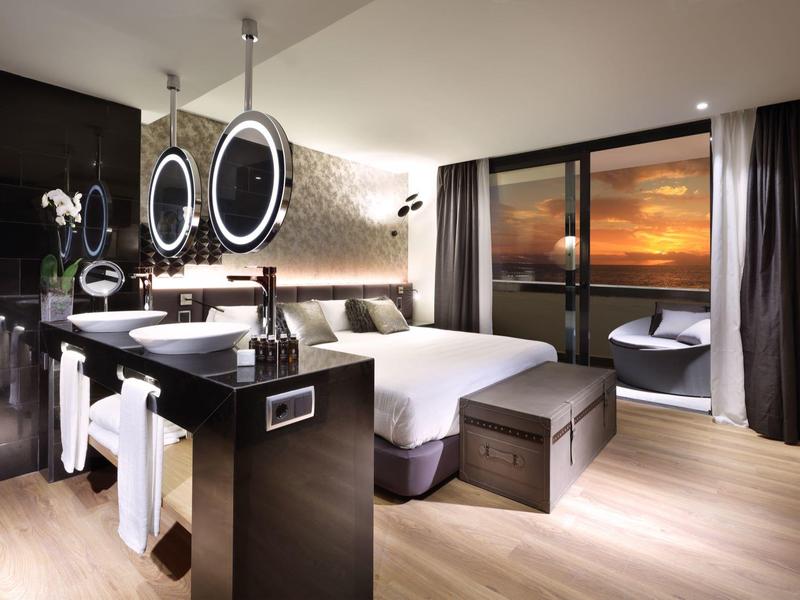 Moderne hotelkamer met groot bed, wastafel met handdoeken en balkon met zonsondergang uitzicht.