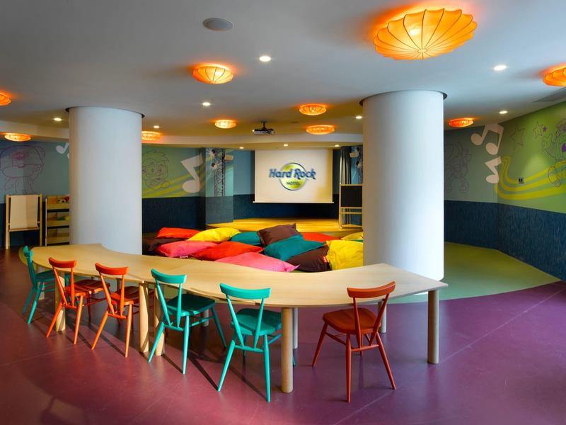 Kleurige stoelen rond een gebogen tafel in een moderne, speelse hotel-lounge met helder licht.