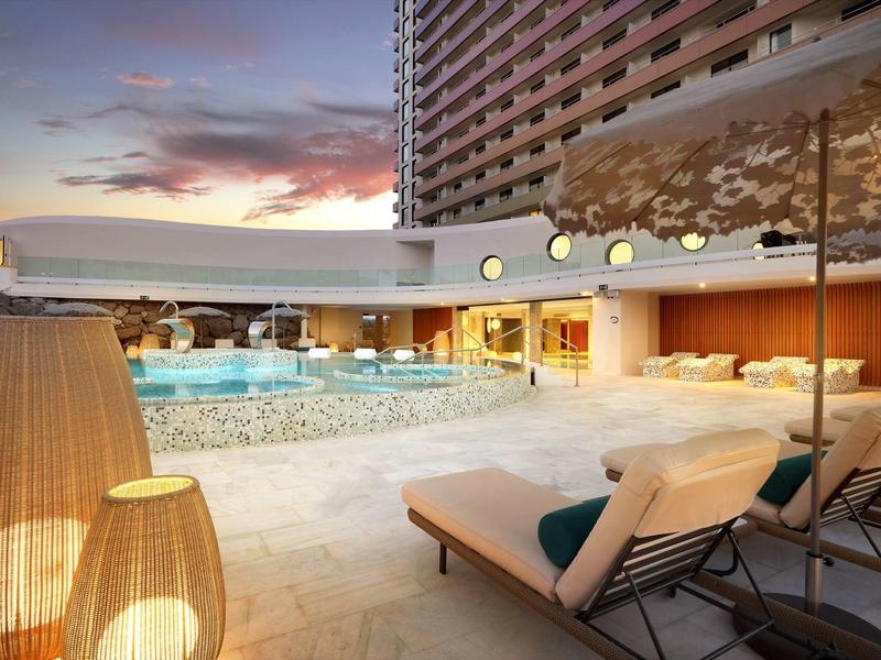 Loungegedeelte bij zwembad met ligbedden, parasol en moderne verlichting bij hotel bij zonsondergang.