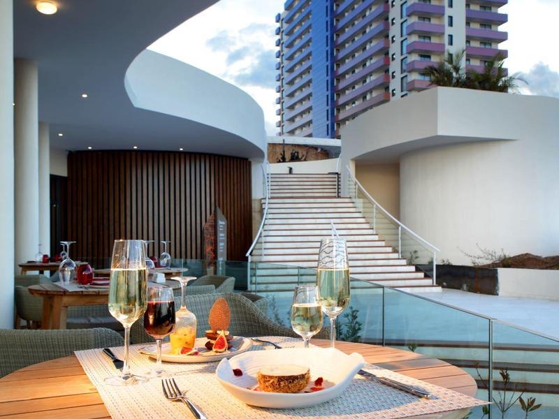 Eettafel met eten bij het zwembad en een hoog hotelgebouw onder een blauwe lucht.