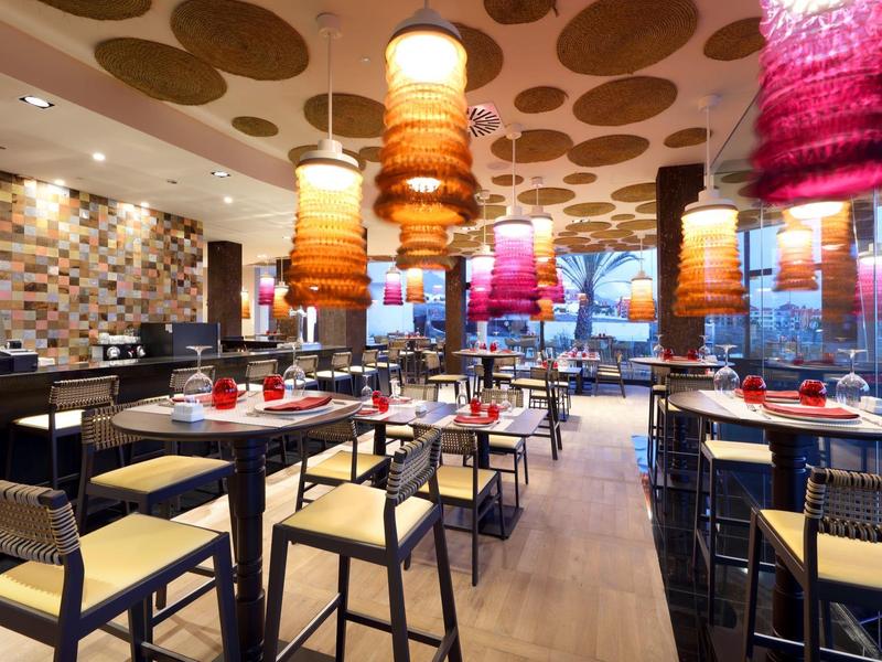 Modern hotelrestaurant met kleurrijke hanglampen en houten meubelen, helder en uitnodigend.