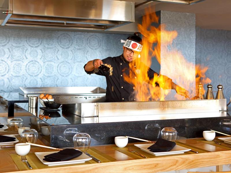 Chef bereidt voedsel met vlammen op een bakplaat in een open keuken.