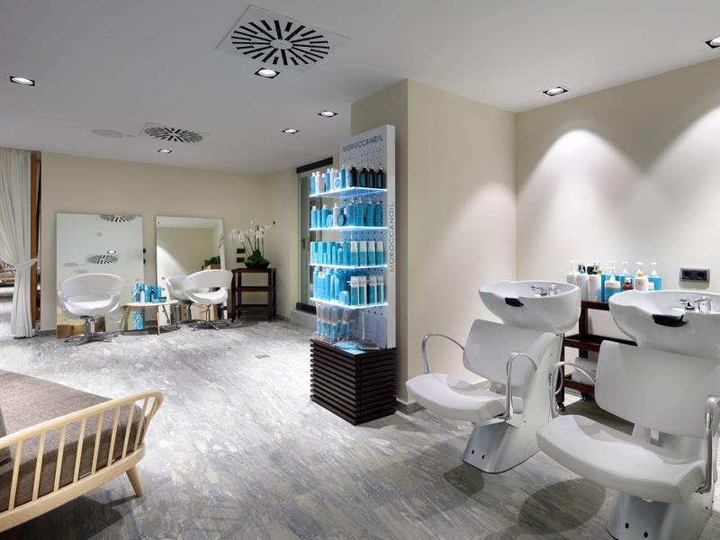 Lichte en moderne spa salon met witte stoelen en planken vol blauwe schoonheidsproducten.