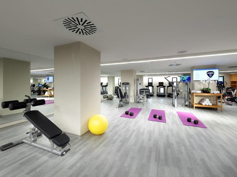 Moderne sportschool met apparatuur, paarse matten en een gele fitnessbal op lichtgrijze vloer.