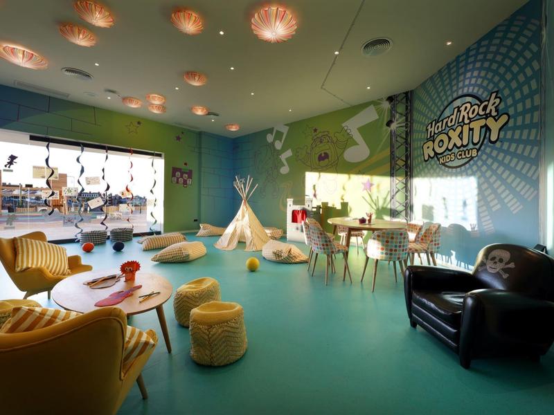 Heldere, kleurrijke speelkamer met tafels, stoelen, tipi en wanddecoraties in een hotelruimte.