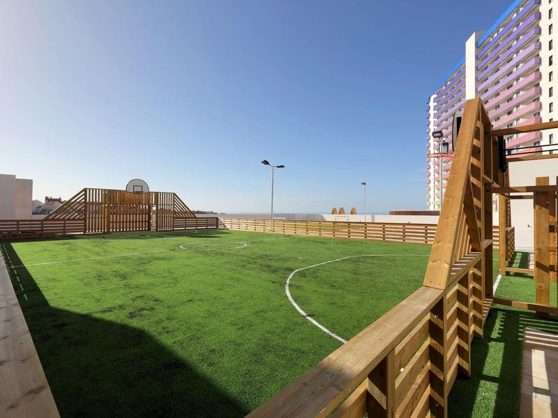 Kleine omheinde voetbalveld met kunstgras op een dakterras onder een heldere lucht.