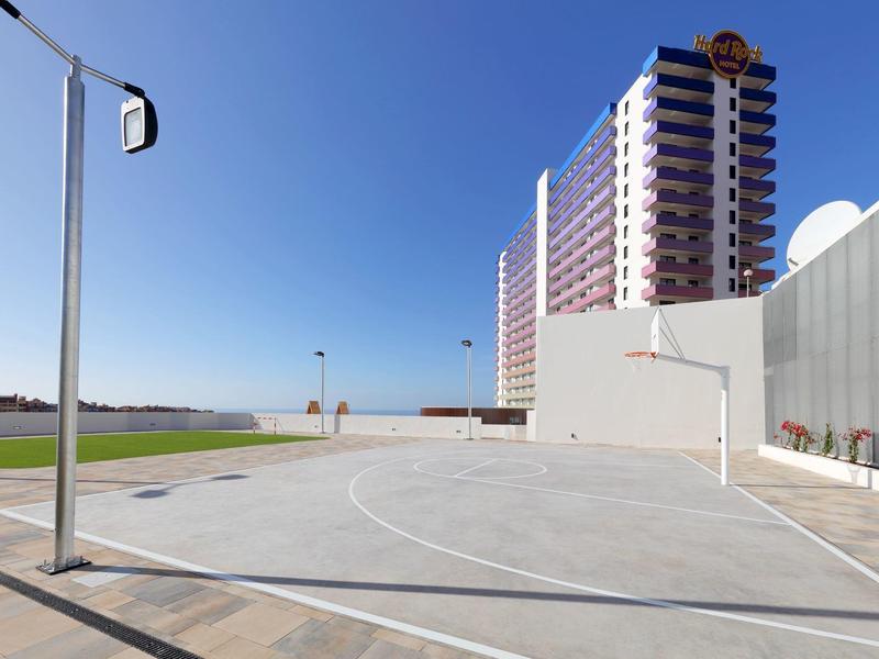 Buiten basketbalveld naast een hoog hotelgebouw onder een heldere blauwe lucht.