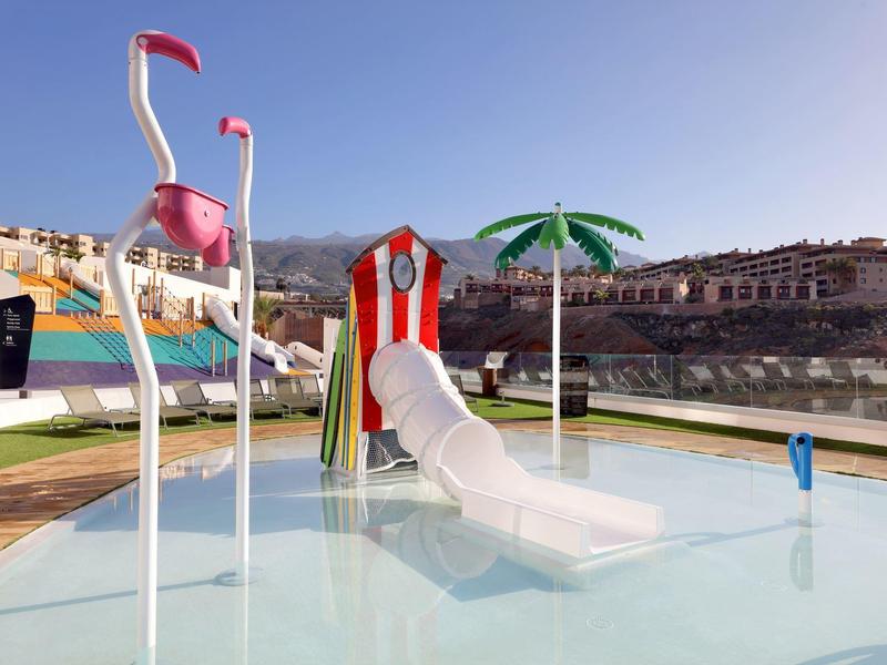 Zwembad met kleurrijke glijbanen en flamingo opblaasbaar in zonnige buitenomgeving.