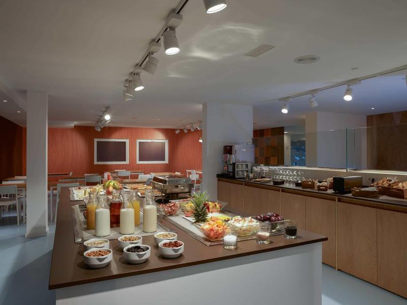 Buffetraum mit vielfältigem Frühstück, Müsli, Obst und Getränken auf Tischen, moderne Beleuchtung.