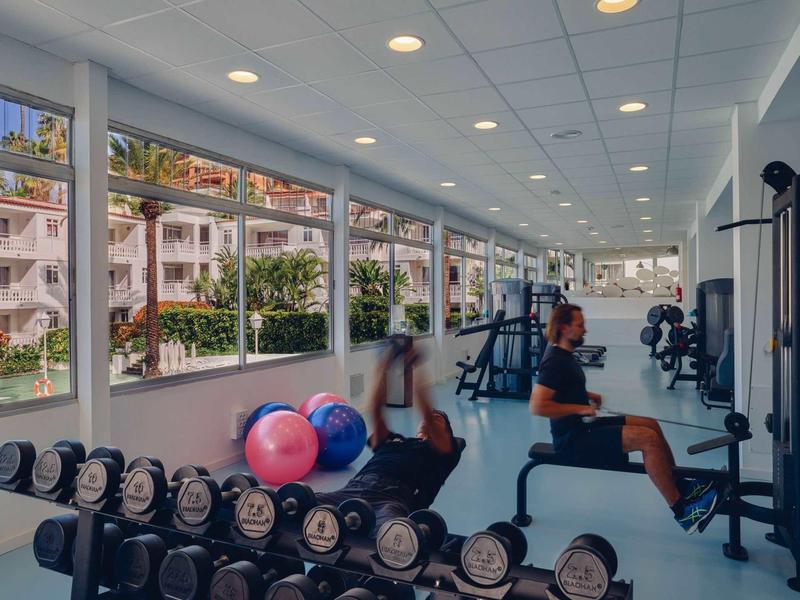 Helles Fitnessstudio mit großen Fenstern, Gewichten, Gymnastikbällen und Sportgeräten.