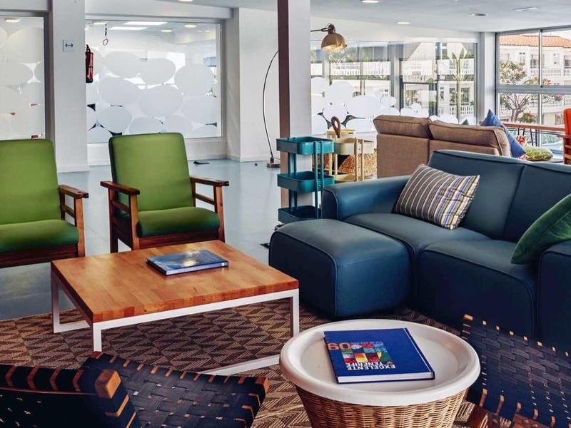 Modern eingerichtetes Wohnzimmer mit blauen Sofas, grünen Sesseln, Holz- und Glasmöbeln.