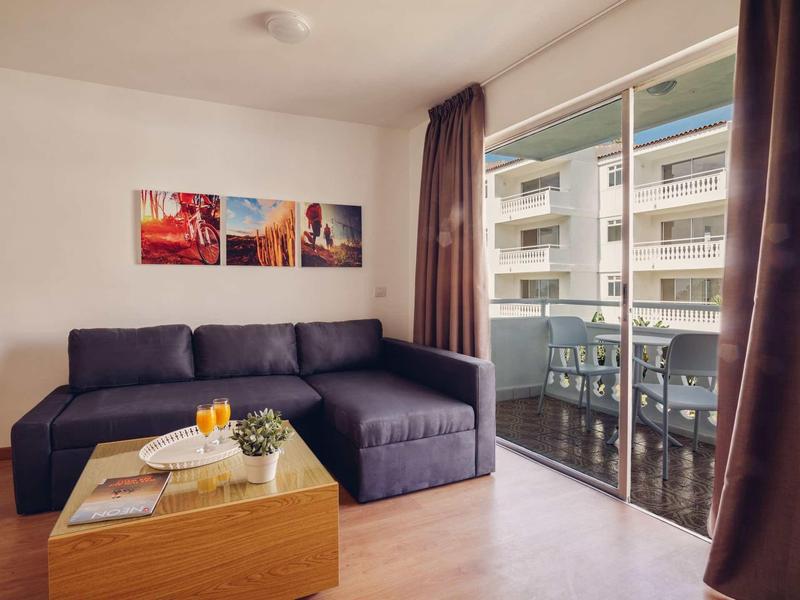 Modernes Wohnzimmer mit dunkelblauem Sofa, Holz-Couchtisch, Pflanzen und großem Balkonfenster.