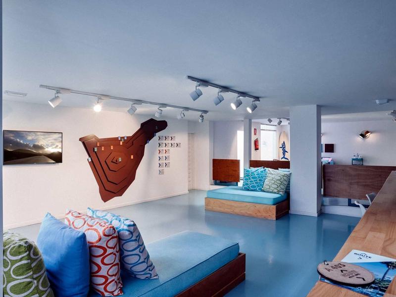 Moderner, heller Raum mit blauer Bodenfläche, bunten Kissen und minimalistischer Holzgestaltung.