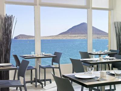 Ristorante moderno con vista sul mare e montagne attraverso grandi finestre.