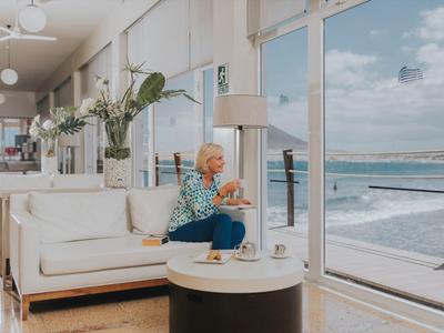 Donna anziana seduta in una stanza d'hotel moderna con vista sul mare.