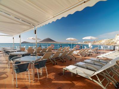 Terrazza con lettini e tavoli sotto tende con vista sul mare.