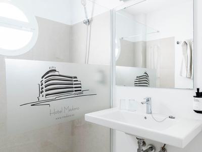 Doccia moderna e luminosa con lavabo bianco, grande specchio e area doccia piastrellata.