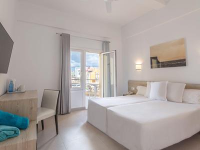 Světlý hotelový pokoj s manželskou postelí, televizí na stěně, psacím stolem a balkonem s výhledem.