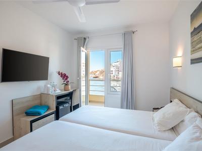 Camera d'albergo luminosa con due letti singoli, TV a parete e vista sul balcone.