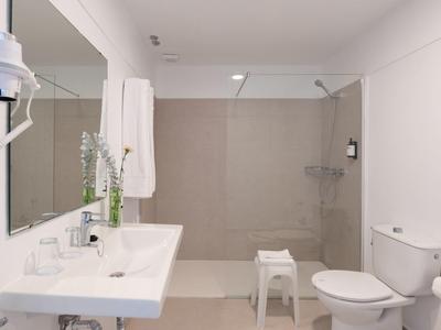 Bagno moderno e luminoso con grande specchio, lavabo, WC e doccia a filo pavimento.