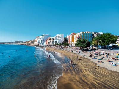 Spiaggia di sabbia con sdraio e hotel lungo la riva sotto un cielo azzurro sereno.