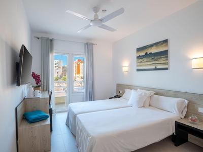 Camera d'hotel moderna con due letti singoli, ventilatore a soffitto e vista sul balcone.