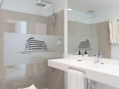 Bagno luminoso con ampia doccia, lavabo, specchio e sgabello di legno con asciugamani.