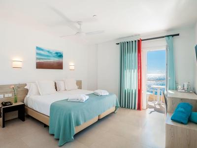 Camera d'hotel luminosa con letto matrimoniale, balcone con vista mare e arredamento moderno.
