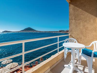 Balcone con tavolo e sedie bianche con vista sul mare blu e cielo limpido.