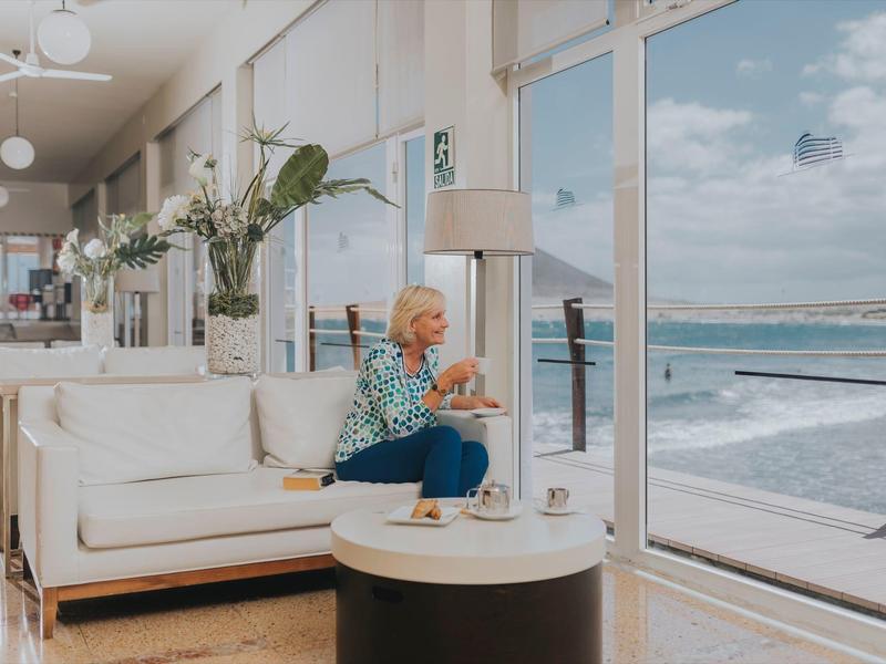 Donna anziana seduta in una stanza d'hotel moderna con vista sul mare.