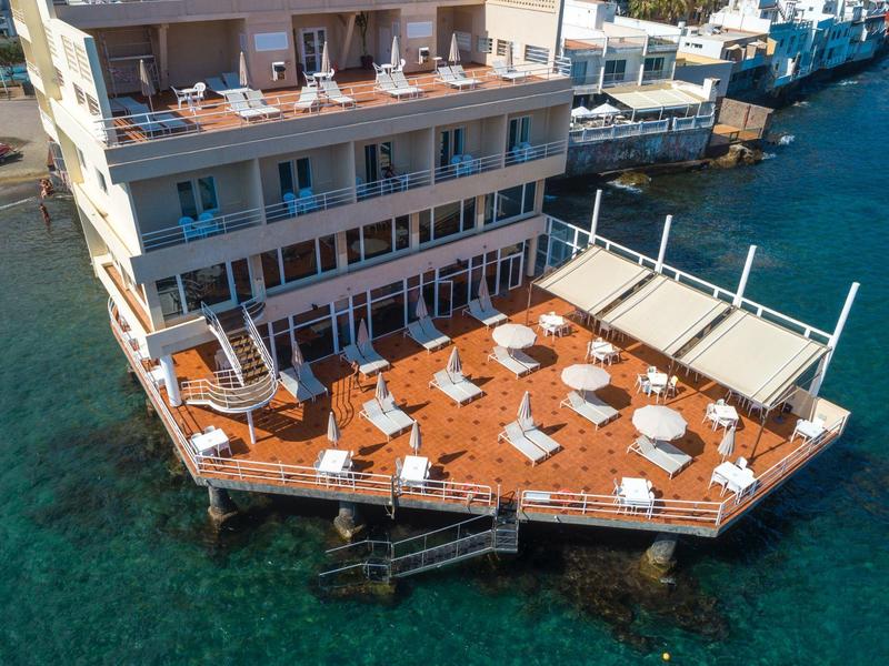 Terrazza dell'hotel con tavoli e sedie bianchi sopra acqua di mare limpida.