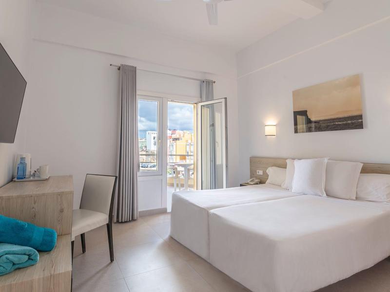 Camera d'hotel luminosa con due letti singoli, scrivania, TV e balcone con vista sulla città