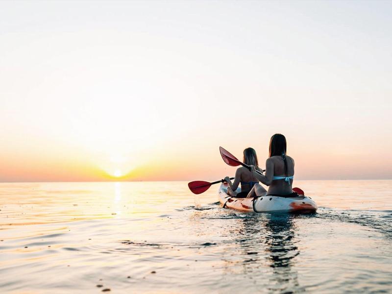 Due persone fanno kayak al tramonto su acque calme.