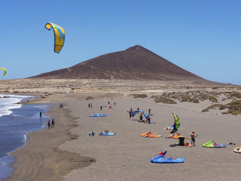 Spiaggia con persone, kitesurf e montagna sullo sfondo sotto un cielo sereno